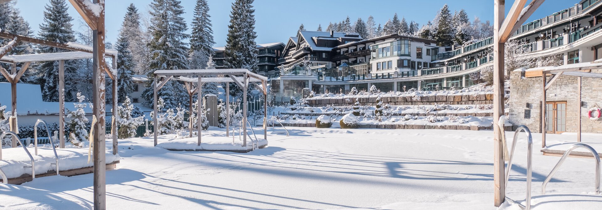 Verschneite Landschaft mit Hotelanlage und Pavillon im Winter unter blauem Himmel