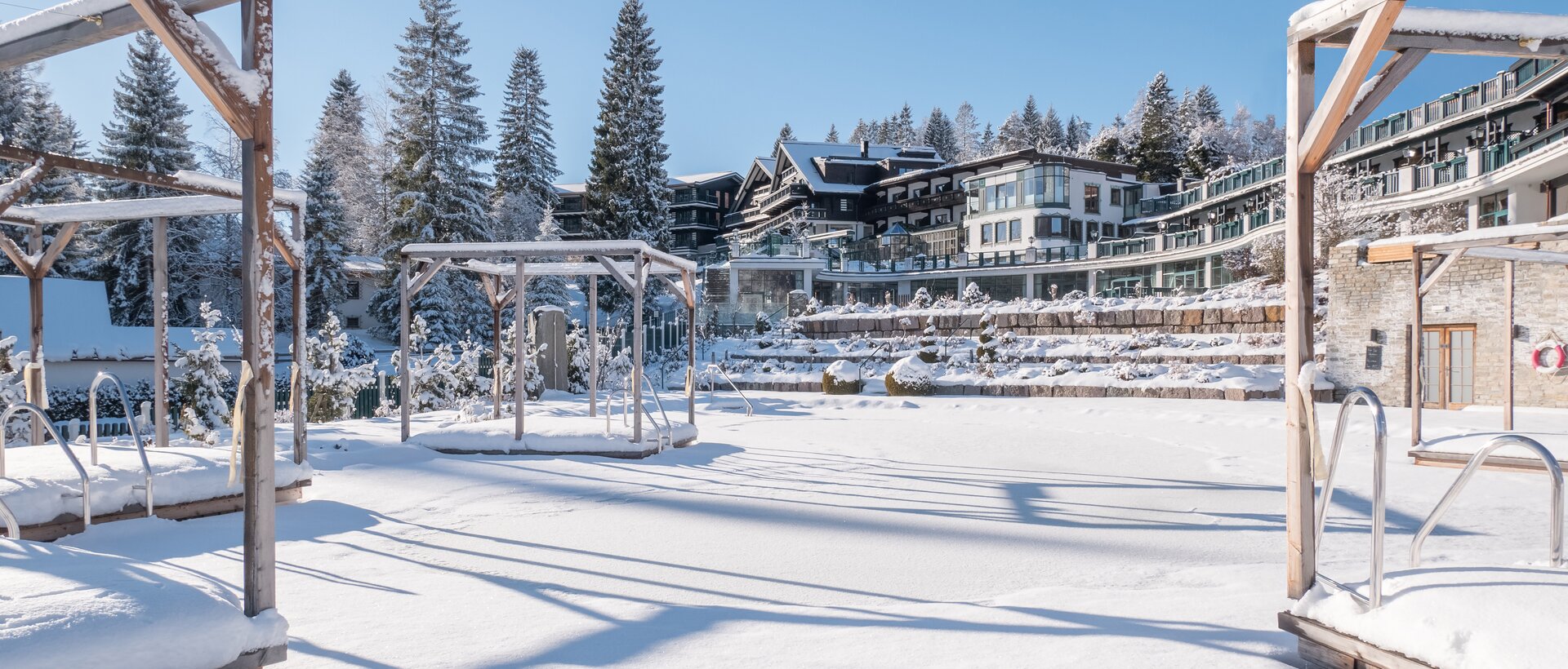 Verschneite Landschaft mit Hotelanlage und Pavillon im Winter unter blauem Himmel