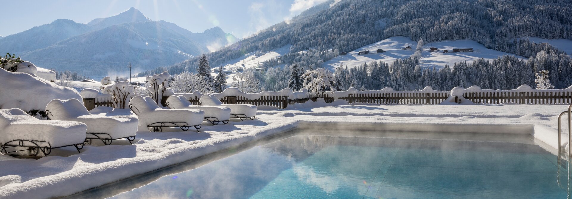Winterlicher Pool vor verschneiter Berglandschaft im Sonnenschein