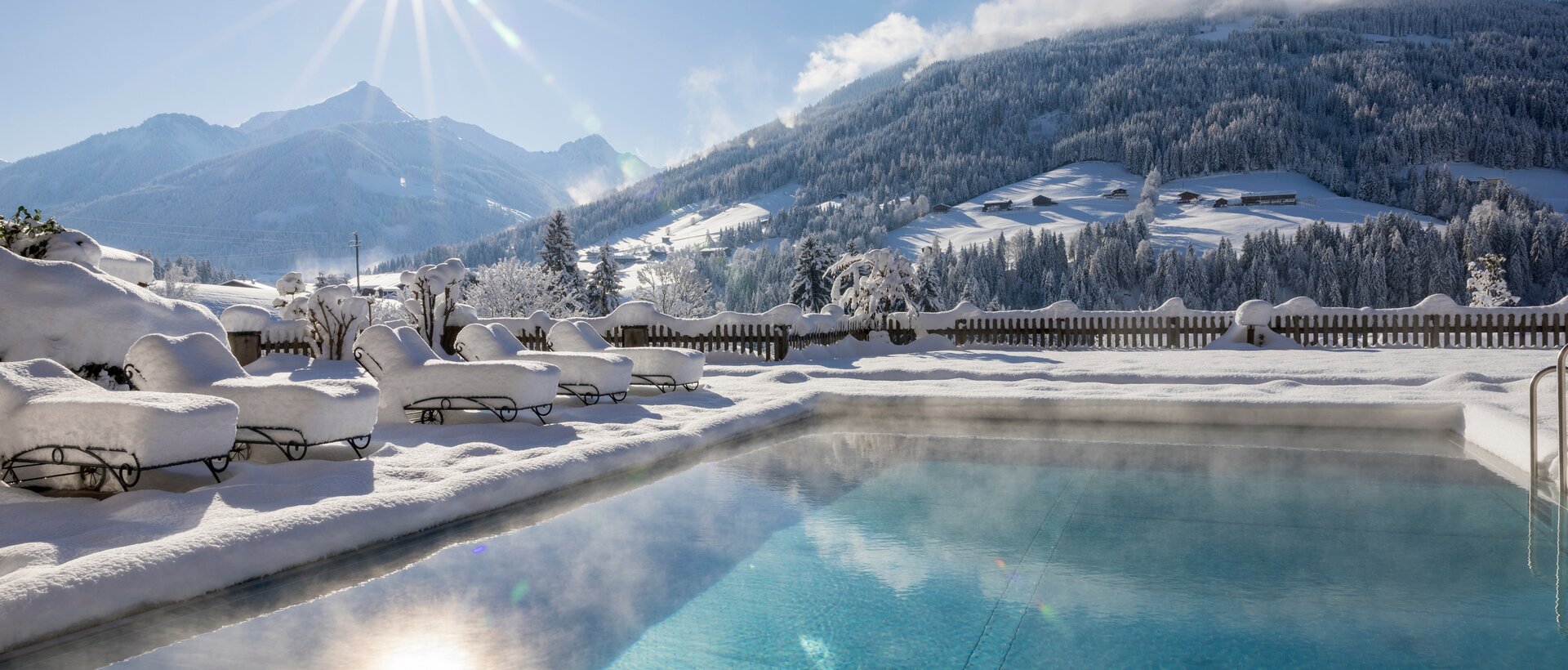Winterlicher Pool vor verschneiter Berglandschaft im Sonnenschein