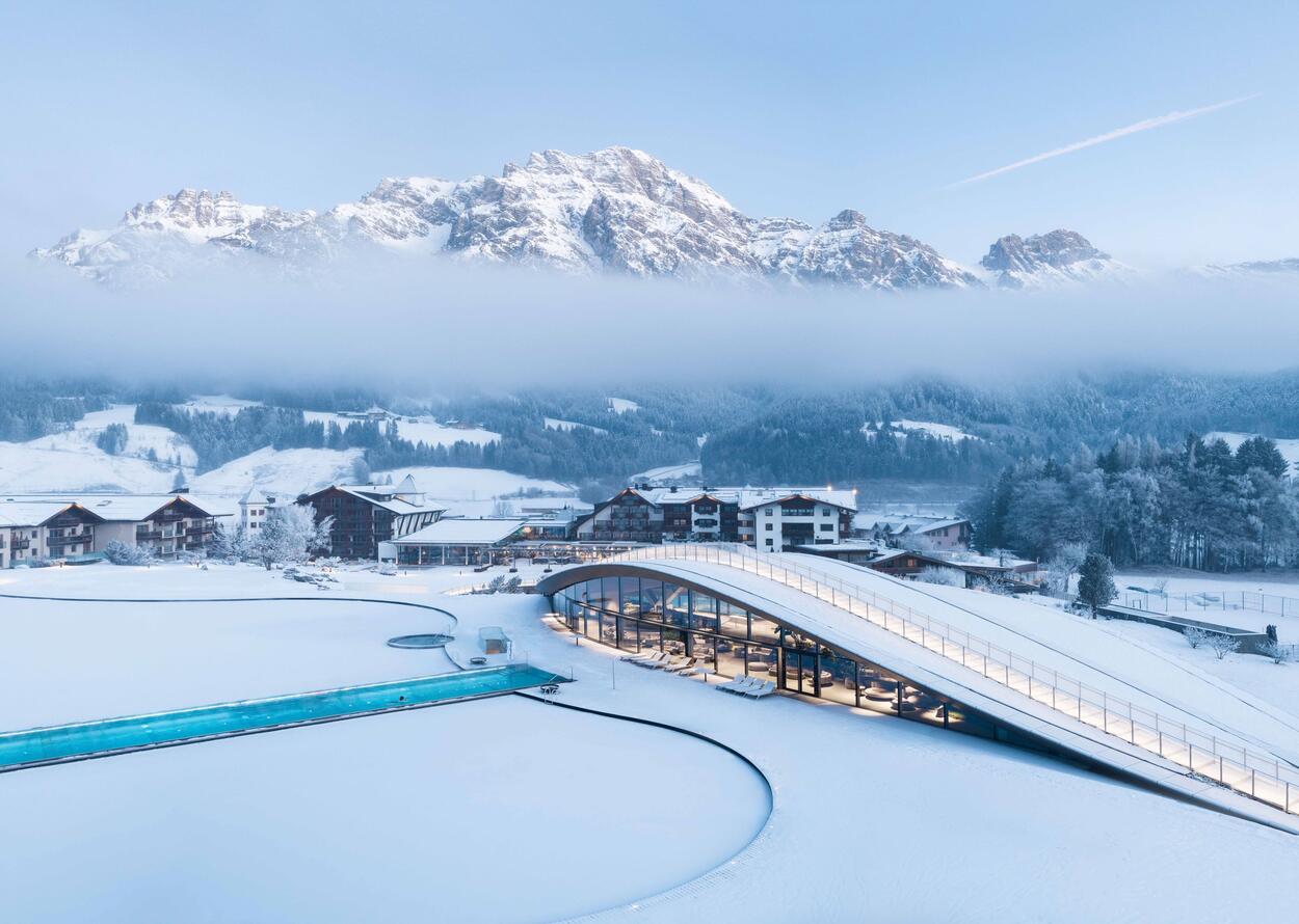 Winterlandschaft mit schneebedeckten Bergen, Häusern und Schwimmbadanlage