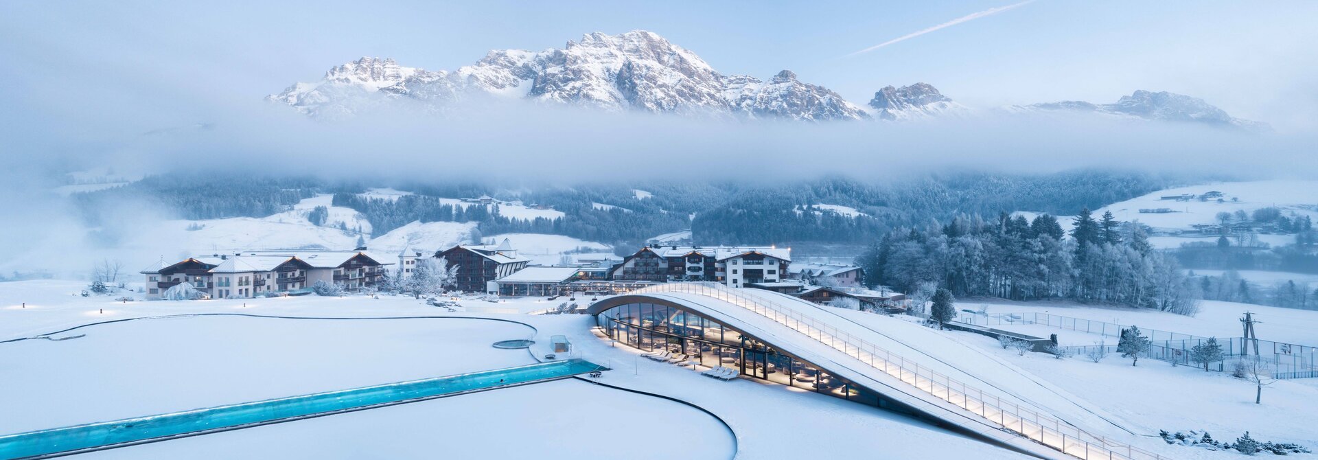 Winterlandschaft mit schneebedeckten Bergen, Häusern und Schwimmbadanlage