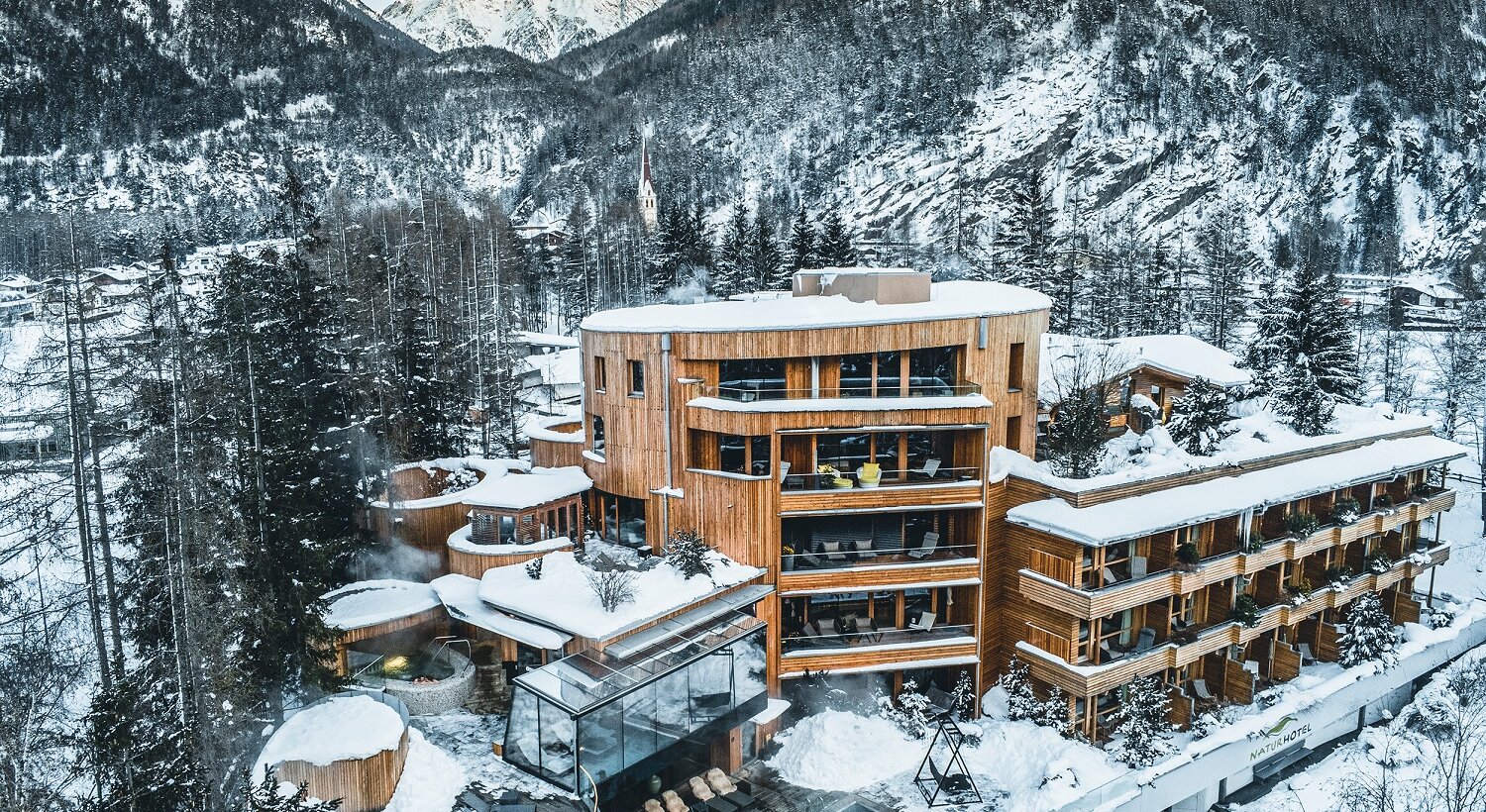 Hotel Waldklause im Winter vor schneebedeckten Bergen mit Pool und Holzbauten