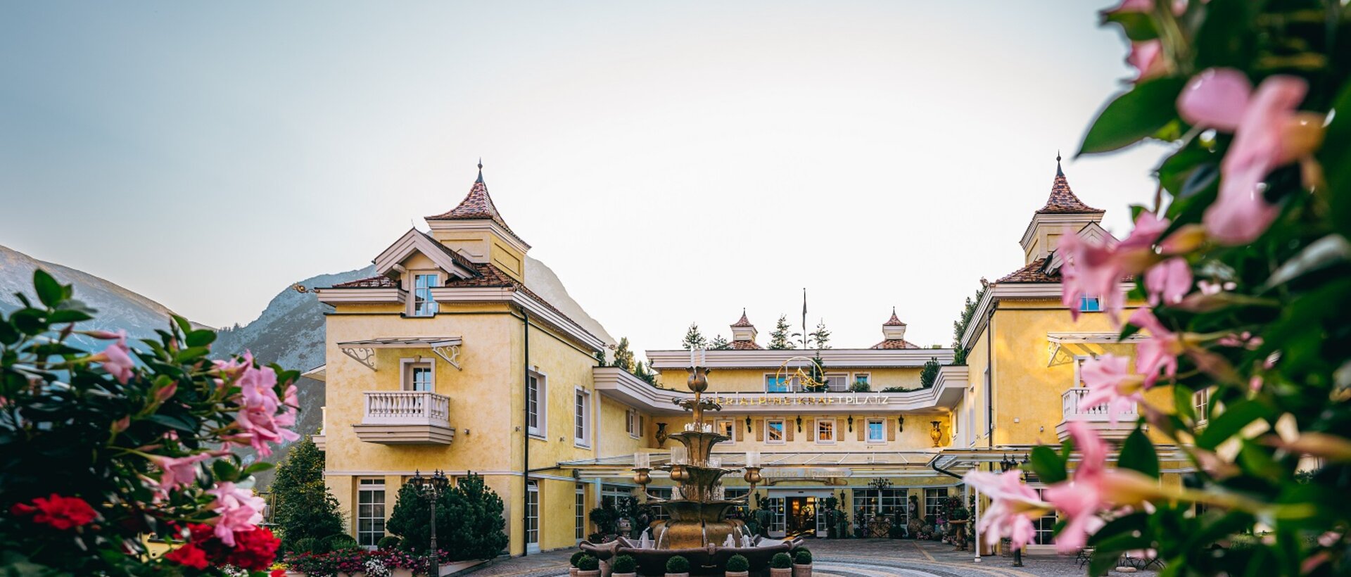 Gelbes Hotelgebäude mit Brunnen im Vordergrund, umrahmt von rosa Blüten