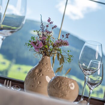 Gedeckter Tisch mit Blumen, Gläsern und Kerze vor Bergpanorama im Speisesaal des Alpbacher Hofs