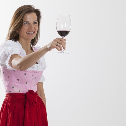 Theresa Egger im Dirndl hält ein Glas Rotwein hoch