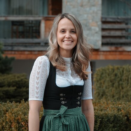 Frau im Dirndl lächelt vor einem Gebäude