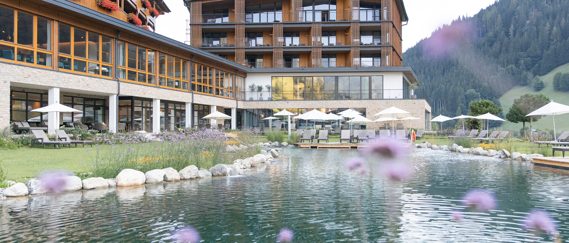 Hotel Nesslerhof mit Teich und Liegewiese im Sommer vor Bergkulisse