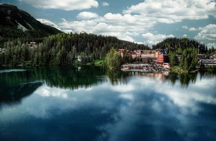 See mit Spiegelung von Wolken, Wald und Häusern am Ufer