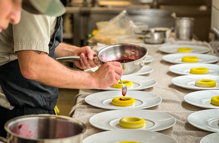In einer professionellen Küche werden mehrere Desserts sorgfältig angerichtet und dekoriert.