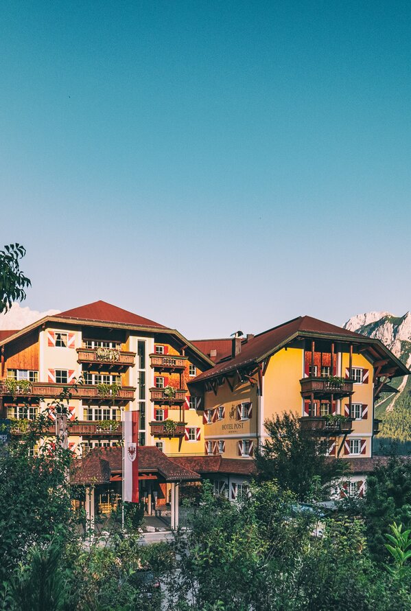 Ein Hotel liegt inmitten einer grünen Landschaft mit Bergen im Hintergrund.