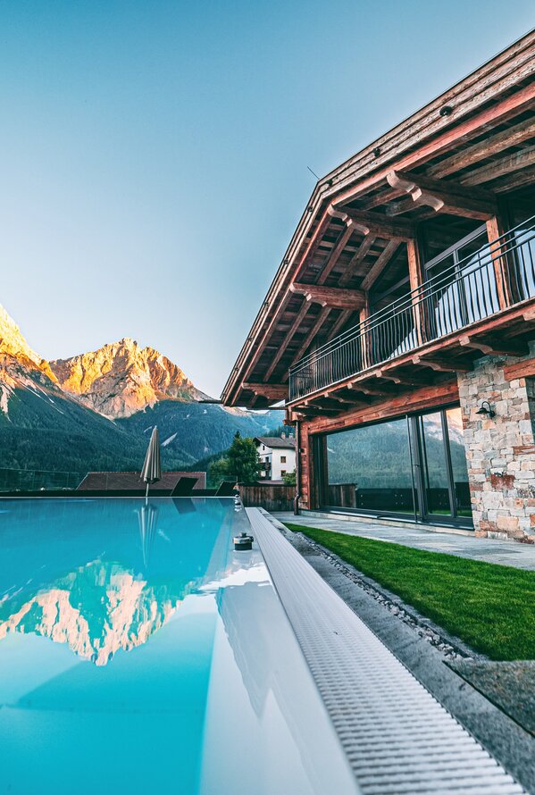 Luxuriöses Bergresort mit Außenpool und beeindruckendem Alpenblick bei Sonnenuntergang.