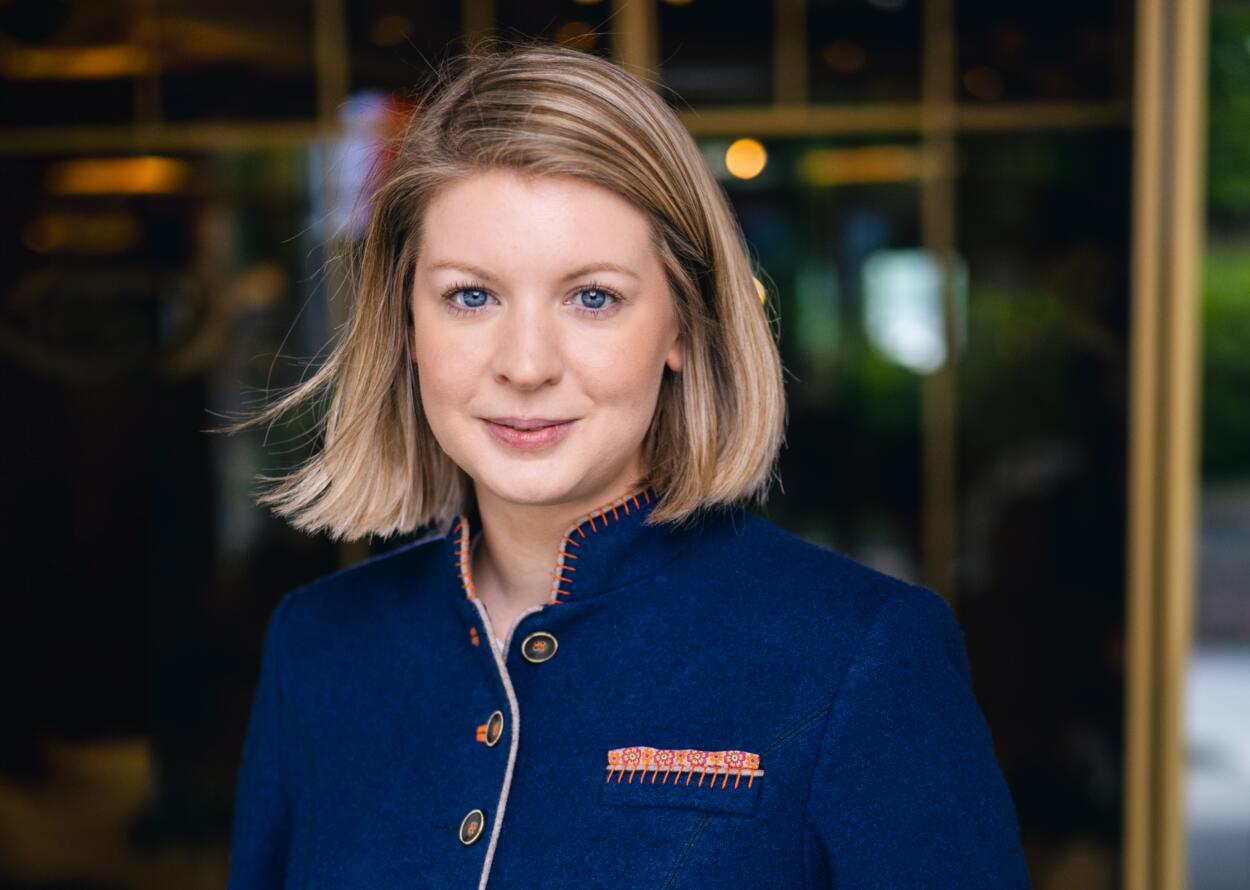 Porträt einer Frau in eleganter, traditionell inspirierter Hotelkleidung vor einem Eingang.