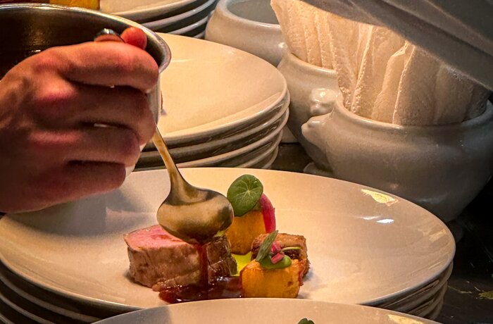 Ein hochwertiges Gericht wird in einer professionellen Küche kunstvoll angerichtet und mit Sauce verfeinert.