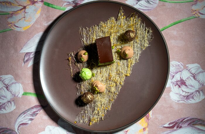 Kreativ angerichtetes Schokoladendessert auf dunklem Teller mit feinen Dekorationen und Pralinen