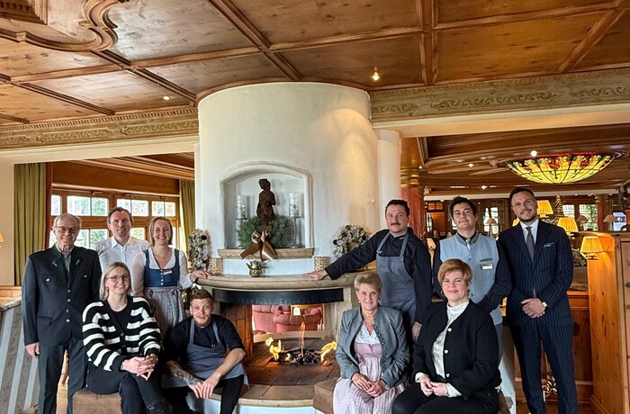 Hotel Alpenrose Teamfoto in festlicher Atmosphäre vor dem Kamin – herzliche Gastfreundschaft und familiäre Tradition