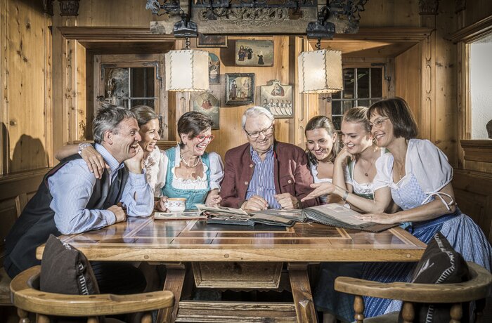 Eine Gruppe von Menschen sitzt gemeinsam in einer gemütlichen Holzhütte und schaut alte Fotos an.