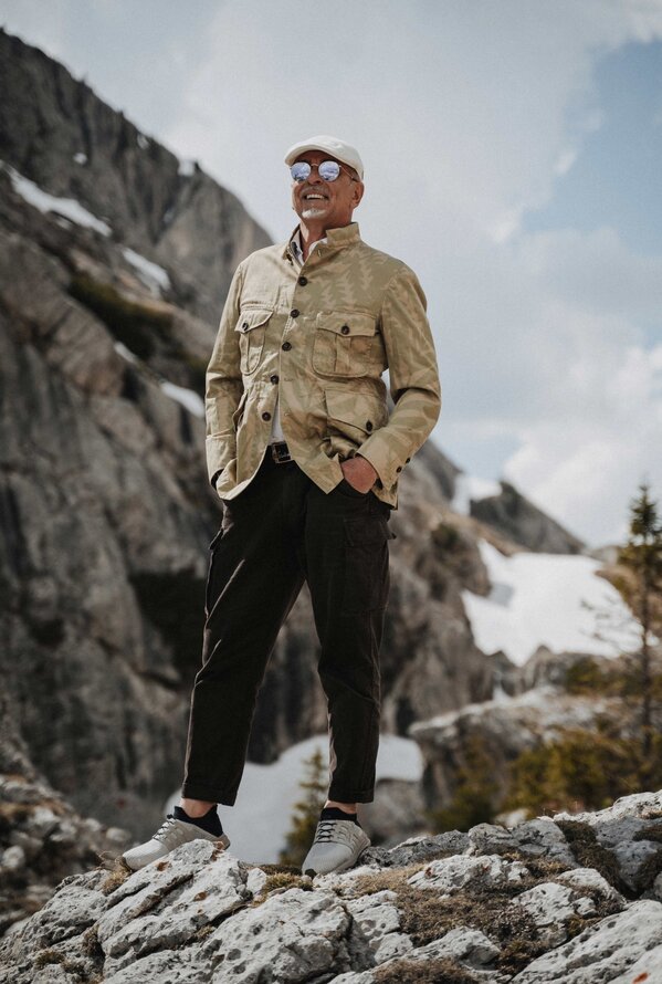 Mann mit Hut, Jacke und Sonnenbrille steht in Berglandschaft
