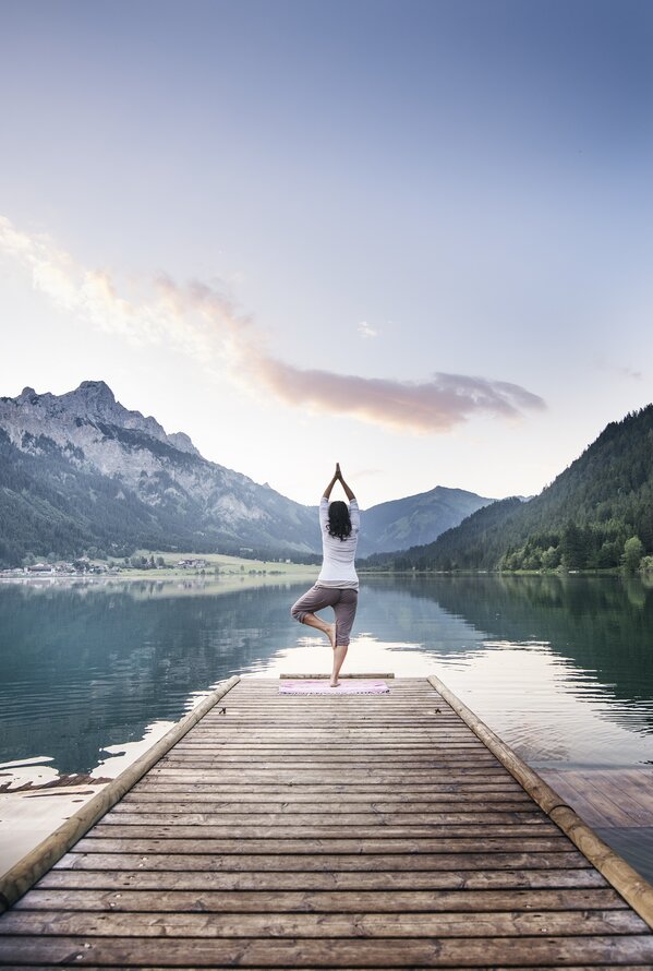 Woman doing yoga on jetty in front of mountain lake