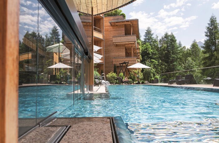 Schwimmbad vor Holzhotel mit Sonnenschirmen und Bäumen