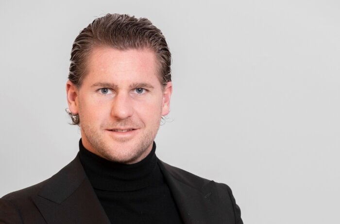 Mann im schwarzen Anzug zeigt auf Smartphone mit Immobilienanzeigen