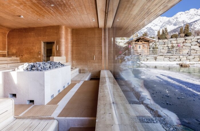 Wood-paneled interior with sauna and view of snow-capped mountains and wooden cabin
