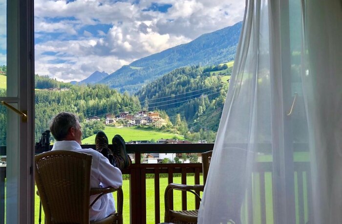 Mann im Bademantel sitzt auf Balkon mit Bergblick