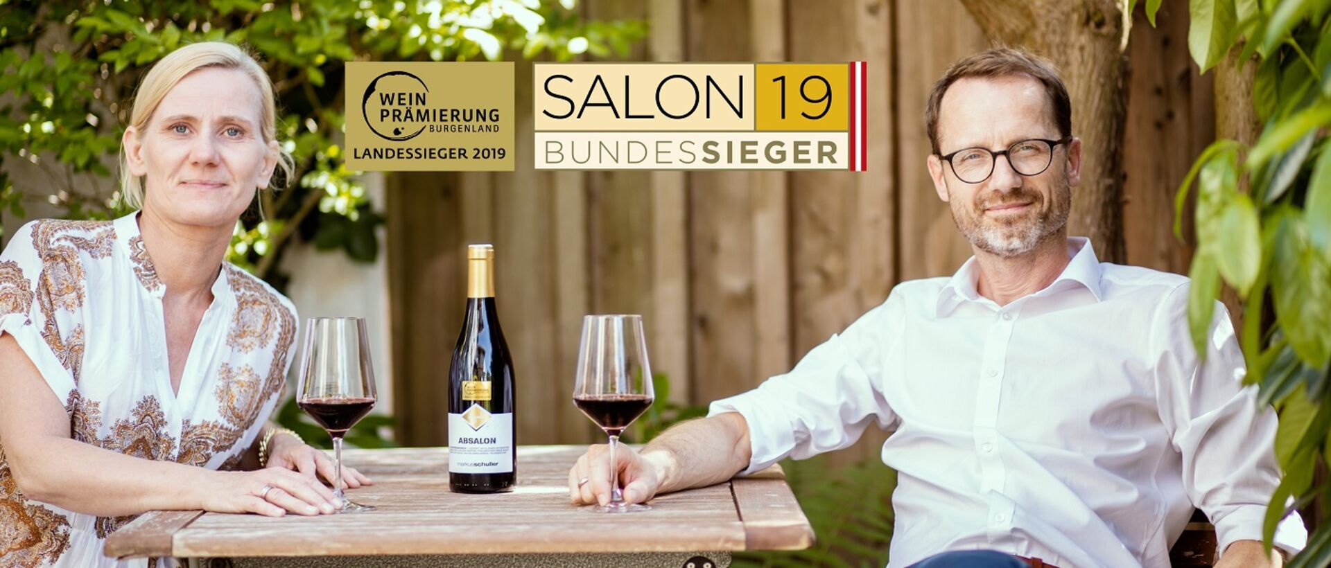 Paar sitzt mit Wein und Auszeichnungen im Garten