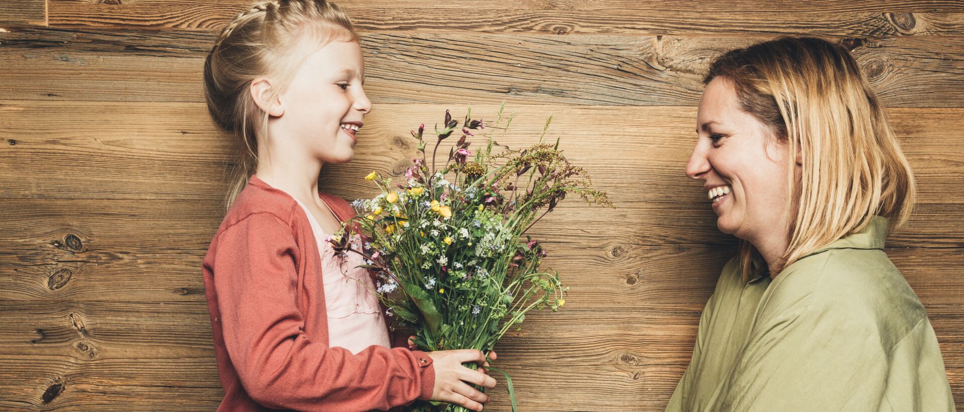Girl gives mother a bouquet of flowers in front of a wooden wall