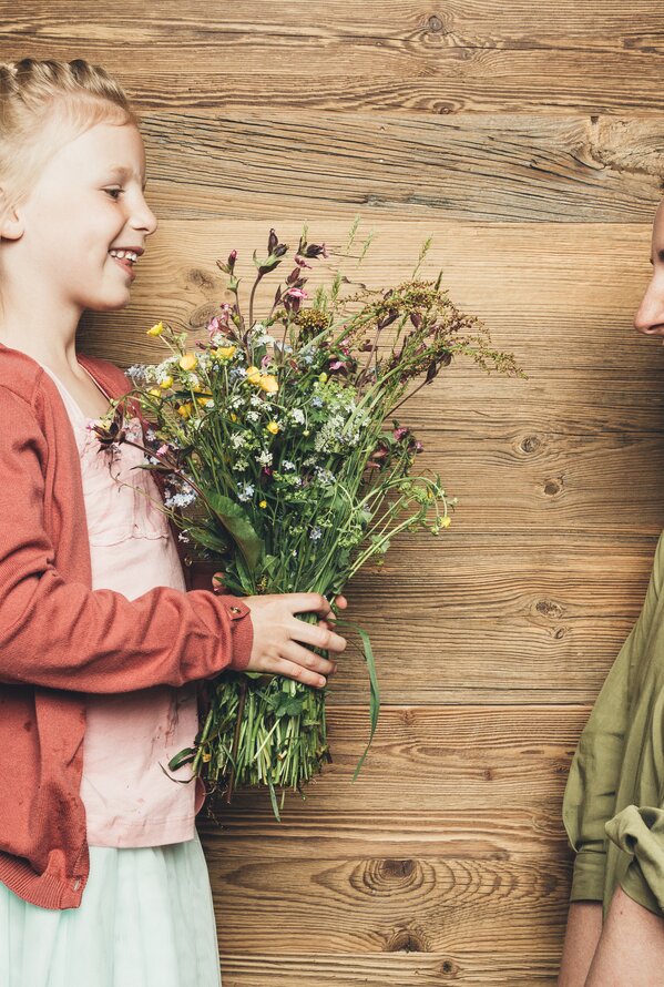 Mädchen schenkt Mutter Blumenstrauß vor Holzwand