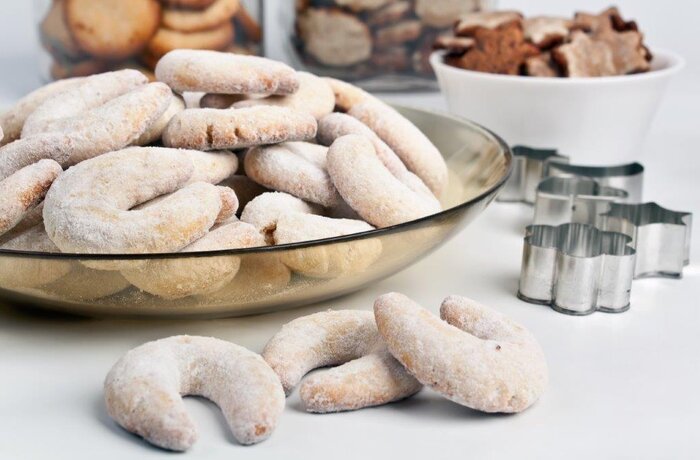 Vanilla crescents in a glass bowl, dusted with icing sugar, cookie cutters in the background