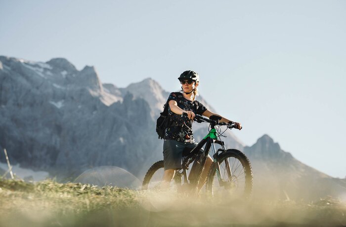 Radfahrer mit Helm und Rucksack auf einem E-Mountainbike vor Bergkulisse