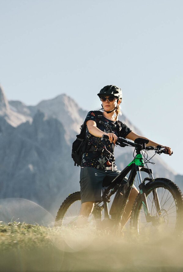 Radfahrer mit Helm und Rucksack auf einem E-Mountainbike vor Bergkulisse