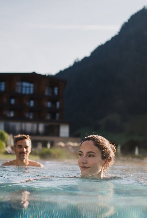 Frau und Mann im Pool vor Bergkulisse und Hotelgebäude