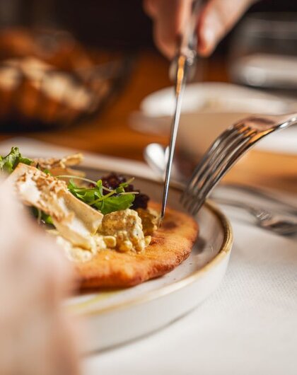 Meal: Person cuts flatbread with topping on plate with knife and fork