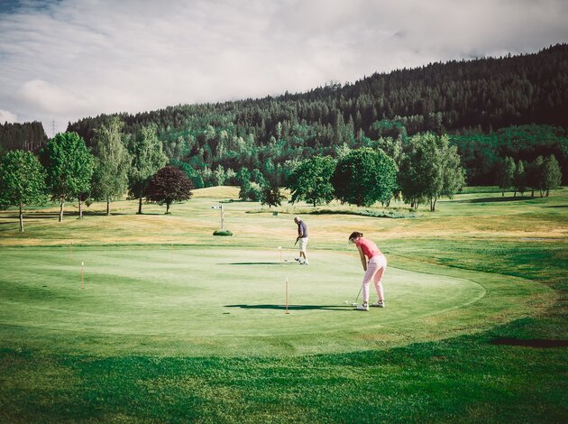 Golfer auf grünem Golfplatz vor bewaldetem Hügel