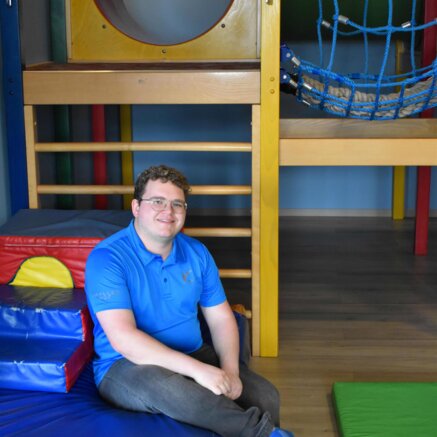 Mann mit Brille und blauem Hemd sitzt in einem Indoor-Spielplatz