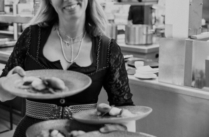 Frau im Dirndl hält Teller mit Speisen in der Hand, lächelt