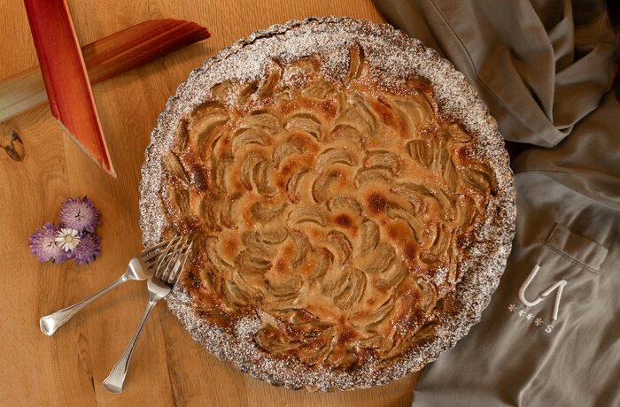 Runde Rhabarbertarte mit Puderzucker und zwei Gabeln auf Holztisch