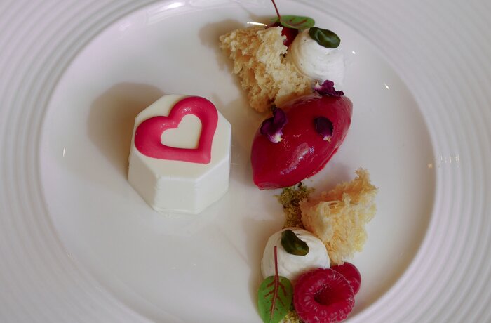 Dessert mit Herz, rotem Sorbet, Baiser und Creme auf weißem Teller
