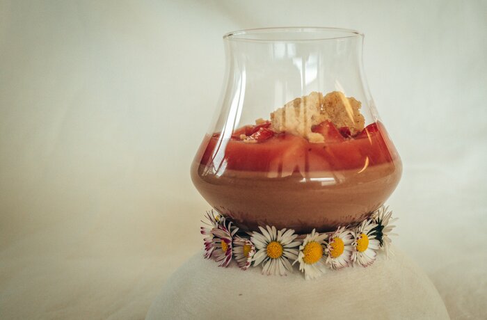Dessert im Glas mit Erdbeeren, Creme und Keks, umrandet von Gänseblümchen