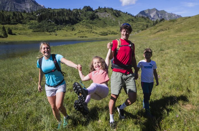 Eine Familie genießt gemeinsam eine Wanderung durch eine idyllische Berglandschaft am See. | © Warth-Schröcken Tourismus / Fotograf: Florian Breitenberger