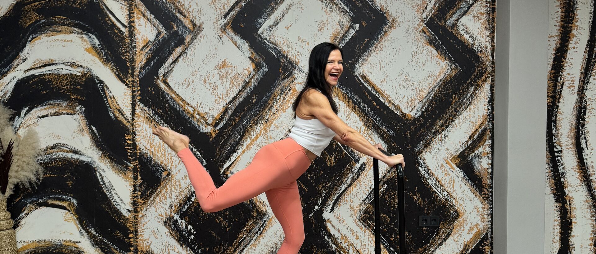 Frau beim Barre-Workout in einem modernen Fitnessstudio mit auffälliger Wandgestaltung.