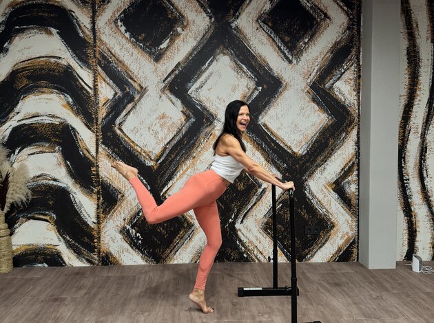 Frau beim Barre-Workout in einem modernen Fitnessstudio mit auffälliger Wandgestaltung.