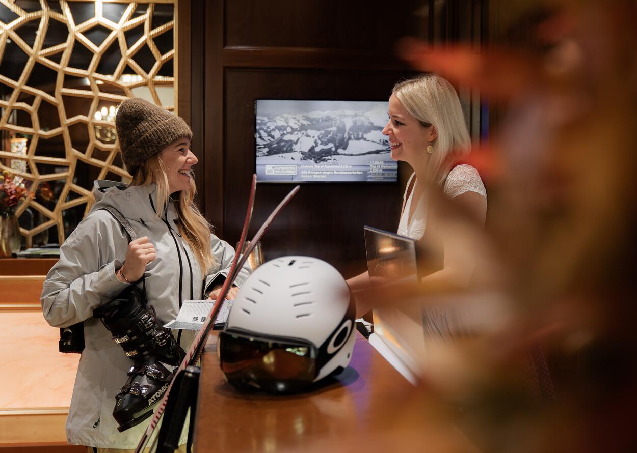 Zwei Frauen an einer Hotelrezeption mit Ski-Equipment.