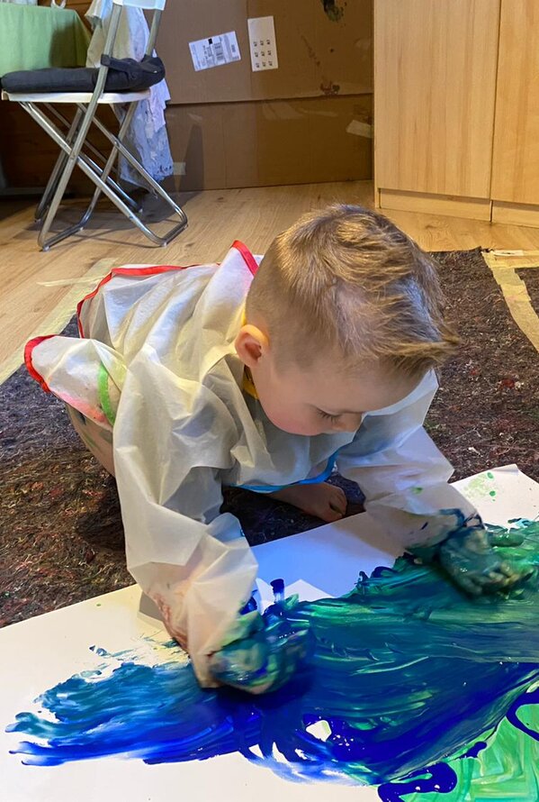 Ein Kind malt mit den Händen bunte Farben auf ein großes Blatt Papier.
