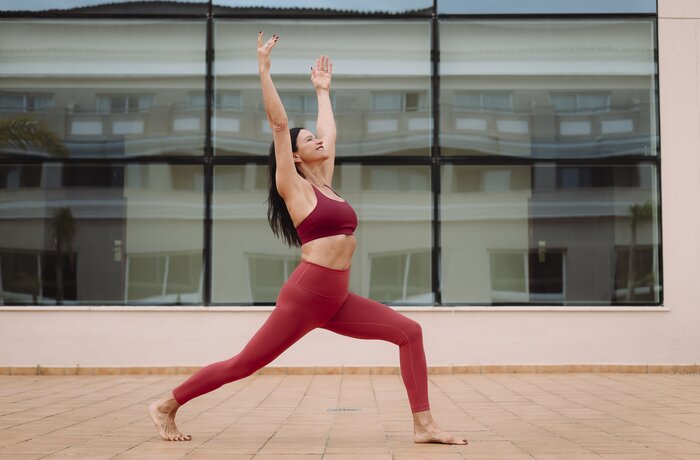 Frau in sportlicher Yoga-Pose auf einer Terrasse vor moderner Glasfassade.