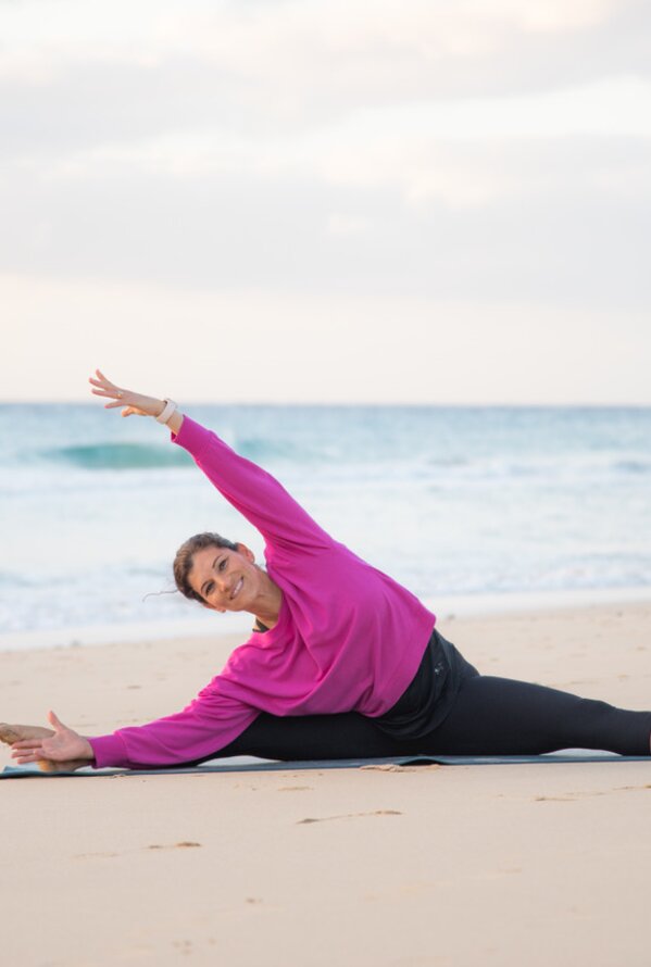 Frau macht Yoga am Strand und dehnt sich entspannt am Meer.