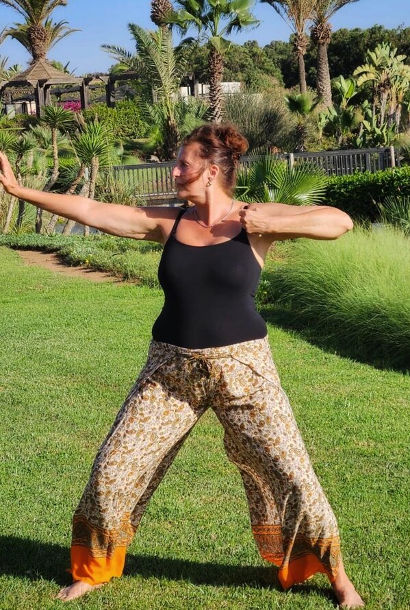 Frau praktiziert Yoga im Freien in einem sonnigen tropischen Garten.