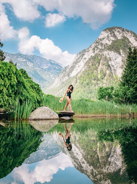 Frau im Badeanzug steht auf Holzsteg am See, Bergpanorama im Hintergrund